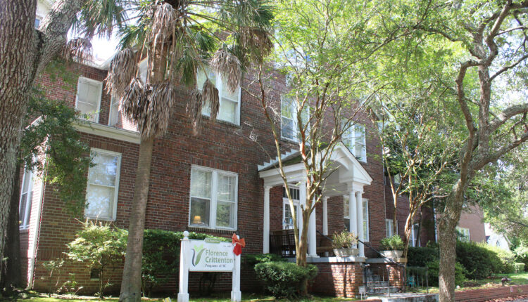 An old brick building with a white sign in front reading "Florence Crittenton Programs of SC" and surrounded by trees.