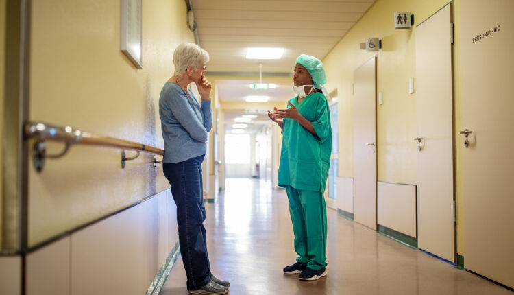 Female surgeon in scrubs talking with senior woman in hospital corridor. Surgeon talking with woman in hallway at hospital.