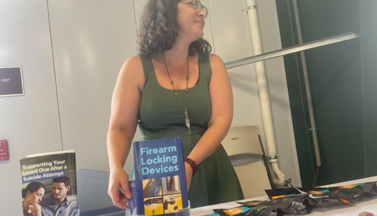 A photo of a woman standing at a table with gun safety pamphlets.