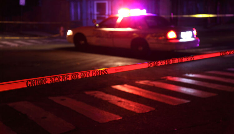 A photo of a police squad car with flashing lights on and crime scene tape in the foreground.
