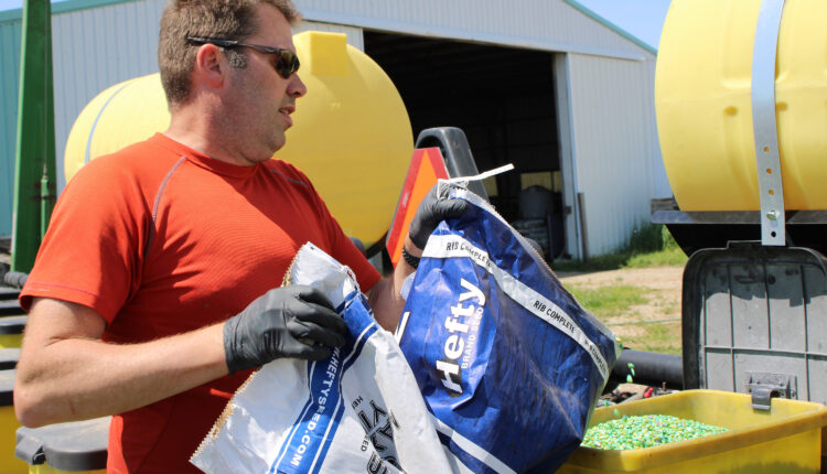 A photo of a farmer placing a seeds into a planter from a large bag.